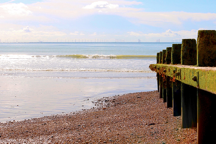 Beach, sea and groyne at low tide (on a sunny day) on the beach looking out to sea towards the Rampion windfarm