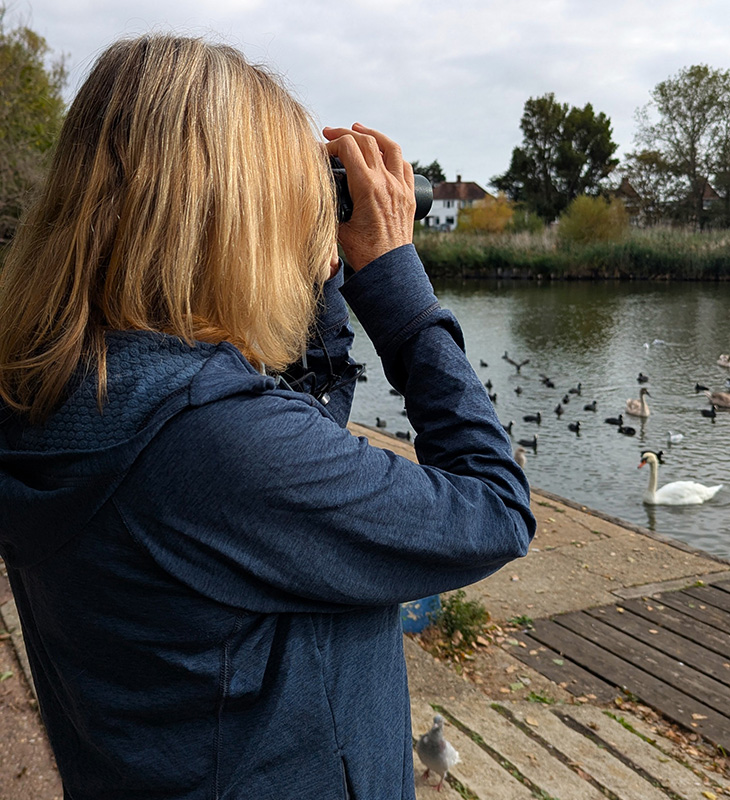 PR26-082 - Jenny Holter, chair of SDOS, using binoculars to look out across the lake at Brooklands Park